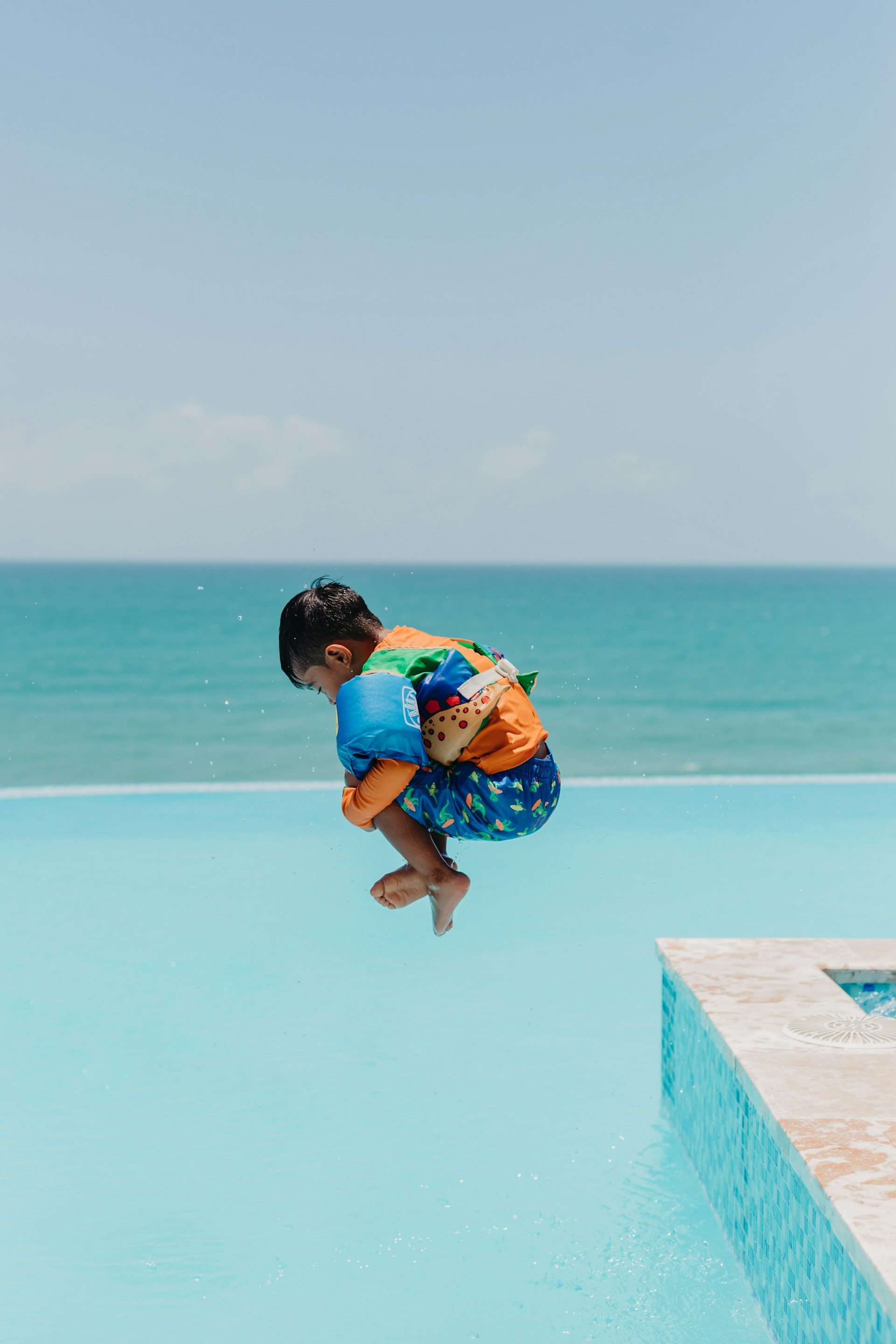 Child mid-jump over an infinity pool with the ocean horizon behind