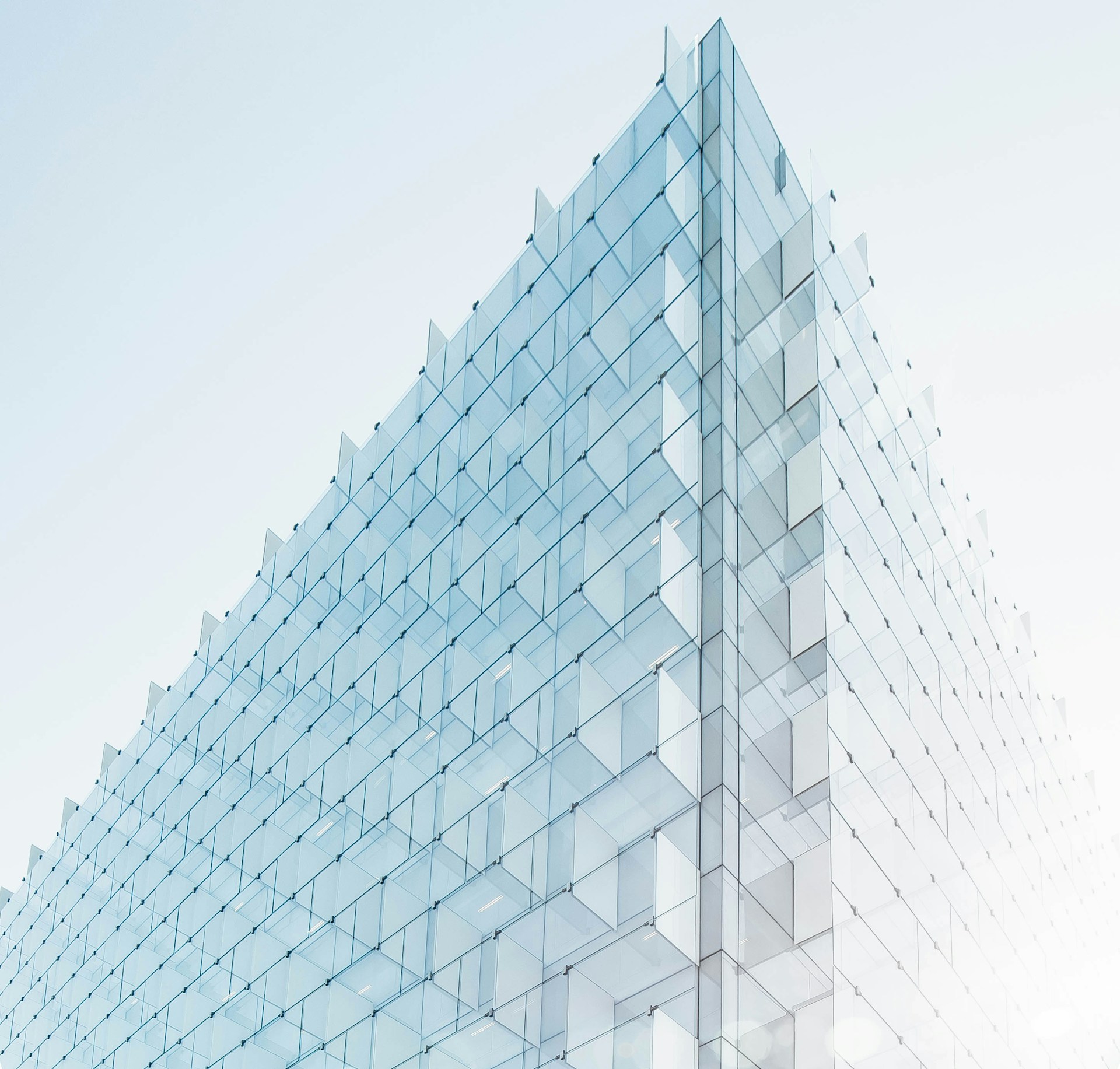 Geometric glass facade reaching into a pale blue sky