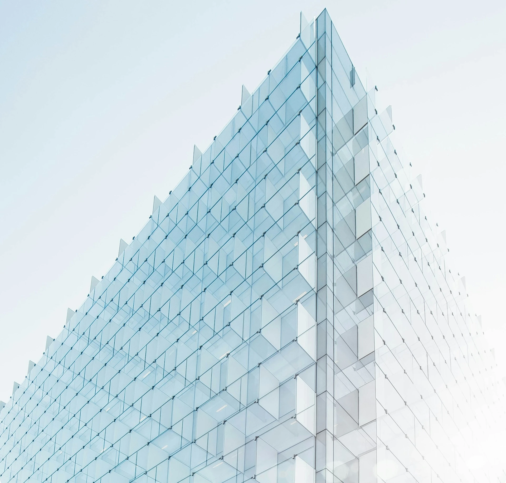 Geometric glass facade reaching into a pale blue sky